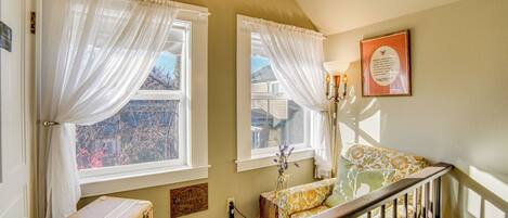 A room with two windows, a staircase, a vintage suitcase, and a framed quote on the wall.