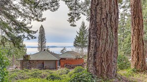 A rustic cabin with a stone chimney, a wooden deck, and a view of a lake and mountains in the background. - Walk to The Oyster Bar: Chuckanut Dr Retreat! (Bow)