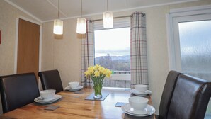 Un coin repas avec une table en bois, quatre chaises, de la vaisselle blanche et un vase rempli de fleurs jaunes.