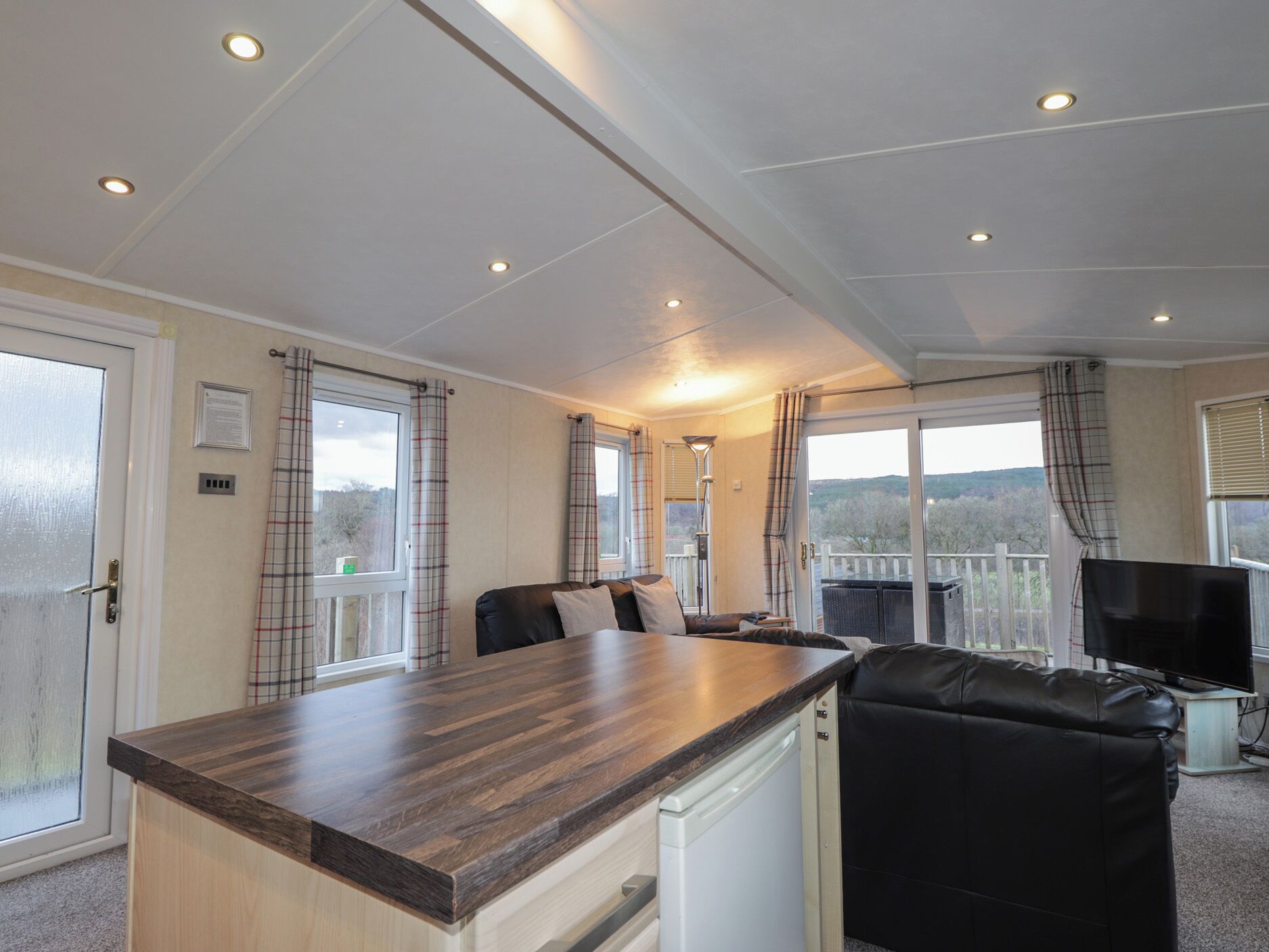 A modern kitchen with a wooden countertop, a built-in dishwasher, and a seating area with a black leather sofa.