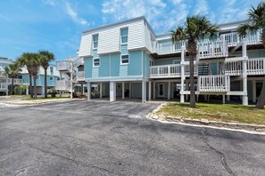 A row of two-story buildings with balconies, a paved driveway, and palm trees. - Fantastic 2-bedroom townhome with great pool and private beach area. (Pensacola Beach)