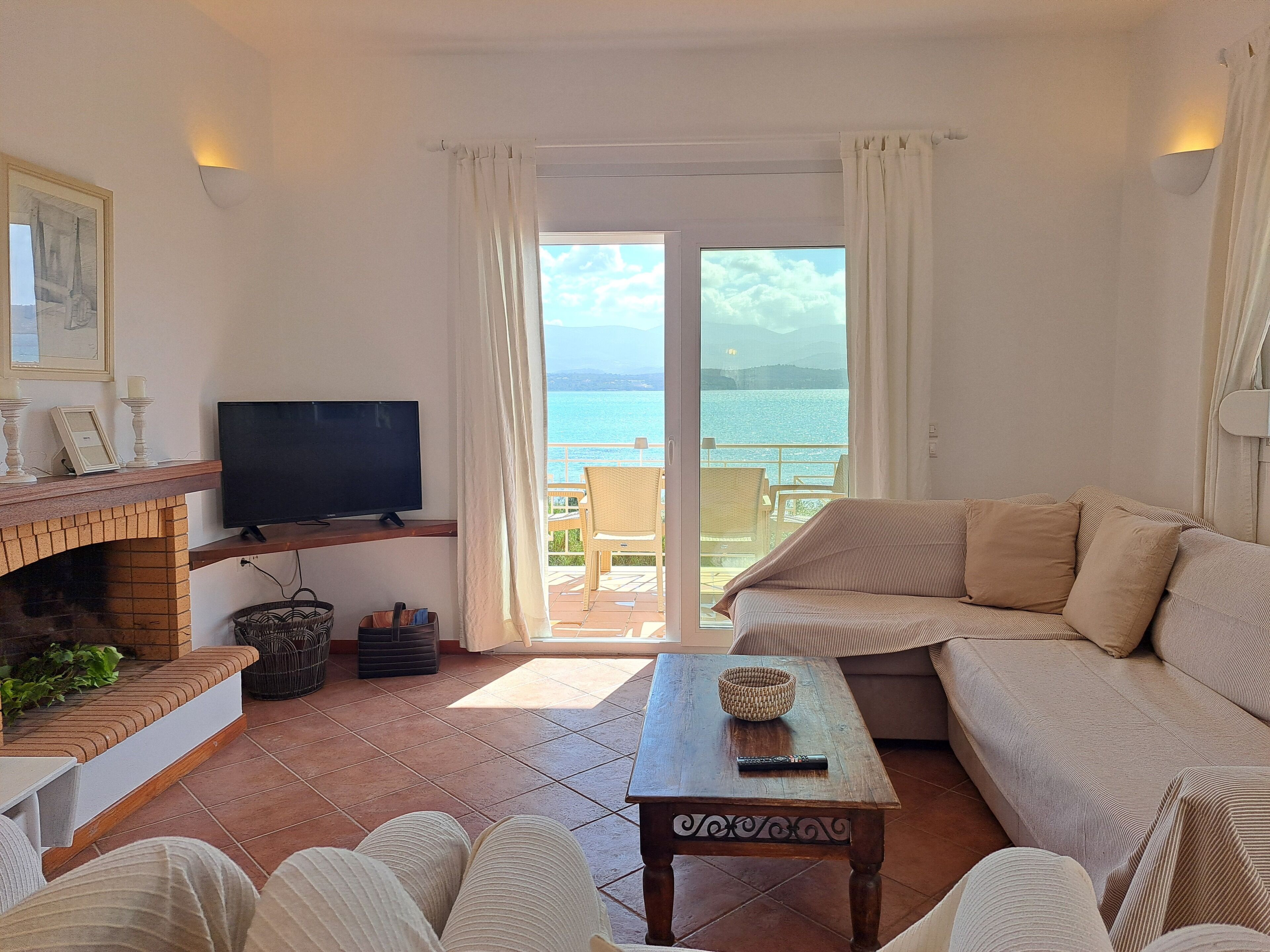 A living room with a TV, sofa, and a view of the sea.