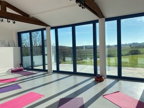 Ein geräumiges Zimmer mit großen Fenstern, Yogamatten und einer Holzzieldecke.