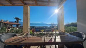 A wooden table with chairs under a pergola, overlooking a scenic view of mountains and a lake.