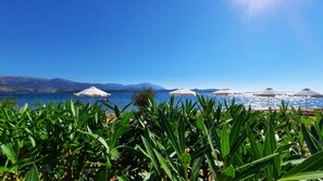 Platja amb sombrerets i un vaixell a l'aigua, envoltada de muntanyes.