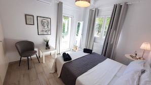 A hotel room with a bed, a chair, a small table with a plant, and a lamp.