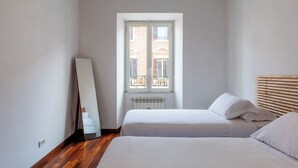 A bedroom with two beds, a window with a view of buildings, and a radiator. - Piazza Alessandria - FromHometoRome (Roma)