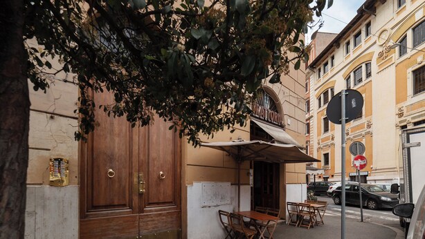 A street-side café with outdoor seating, a large wooden door, and a signboard. - Piazza Alessandria - FromHometoRome (Roma)