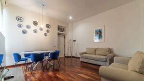 A modern living room with a wooden floor, a dining table with blue chairs, a beige sofa, and a painting on the wall. - Piazza Alessandria - FromHometoRome (Roma)