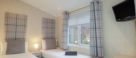 A hotel room with two beds, a TV, and a window with curtains.