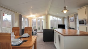 A spacious kitchen with a wooden island, a dining area with chairs and a table set for two, and a black sofa. - Islay Lodge (Spean Bridge)