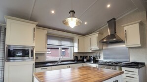 A modern kitchen with white cabinetry, a wooden island, stainless steel appliances, and a window with blinds. - Islay Lodge (Spean Bridge)