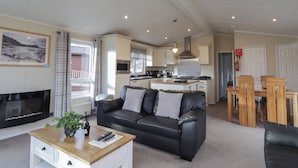 A modern living room with a black leather sofa, a wooden coffee table, and a fireplace. - Islay Lodge (Spean Bridge)