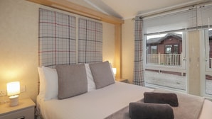 A hotel room with a bed, bedside lamps, a window with a view of a building, and a balcony with a railing. - Islay Lodge (Spean Bridge)