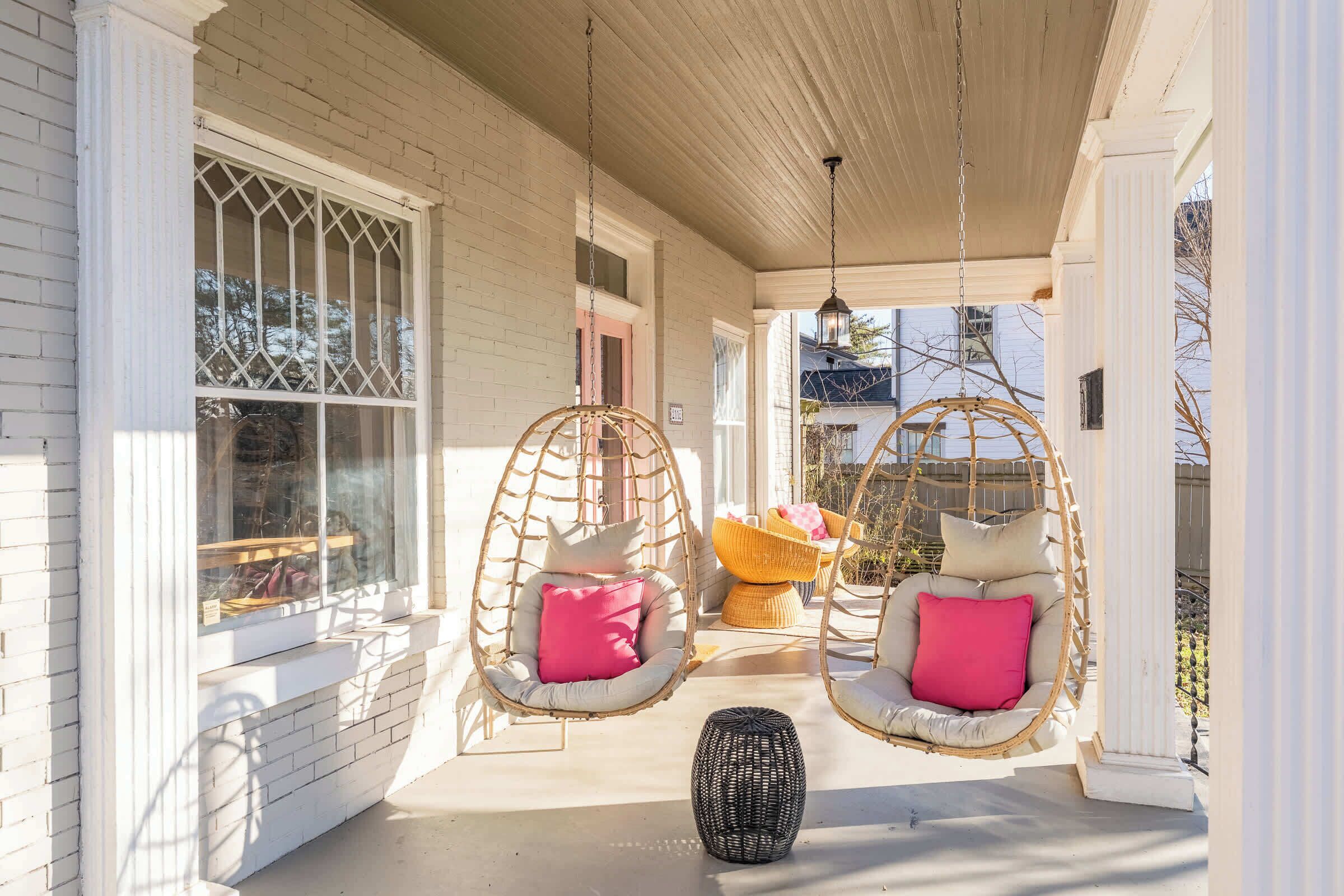 A porch with two wicker swing chairs, a wicker table, and a hanging lantern.