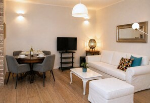 A living room with a dining table, chairs, a sofa, a coffee table, a TV, and a lamp. - Thomais House – Spacious Family Home with Private Garden Near Corfu Old Town & Beach (Κέρκυρα)