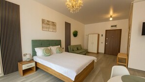A bedroom with a large bed, a nightstand, a green sofa, a wooden wardrobe, and a television on the wall. - Sasha Collection at N10 by Alezzi (Mamaia-Sat)