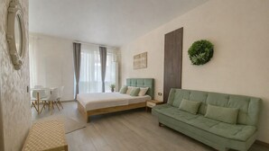 A modern bedroom with a bed, a green sofa, a dining table, and a small table. - Sasha Collection at N10 by Alezzi (Mamaia-Sat)
