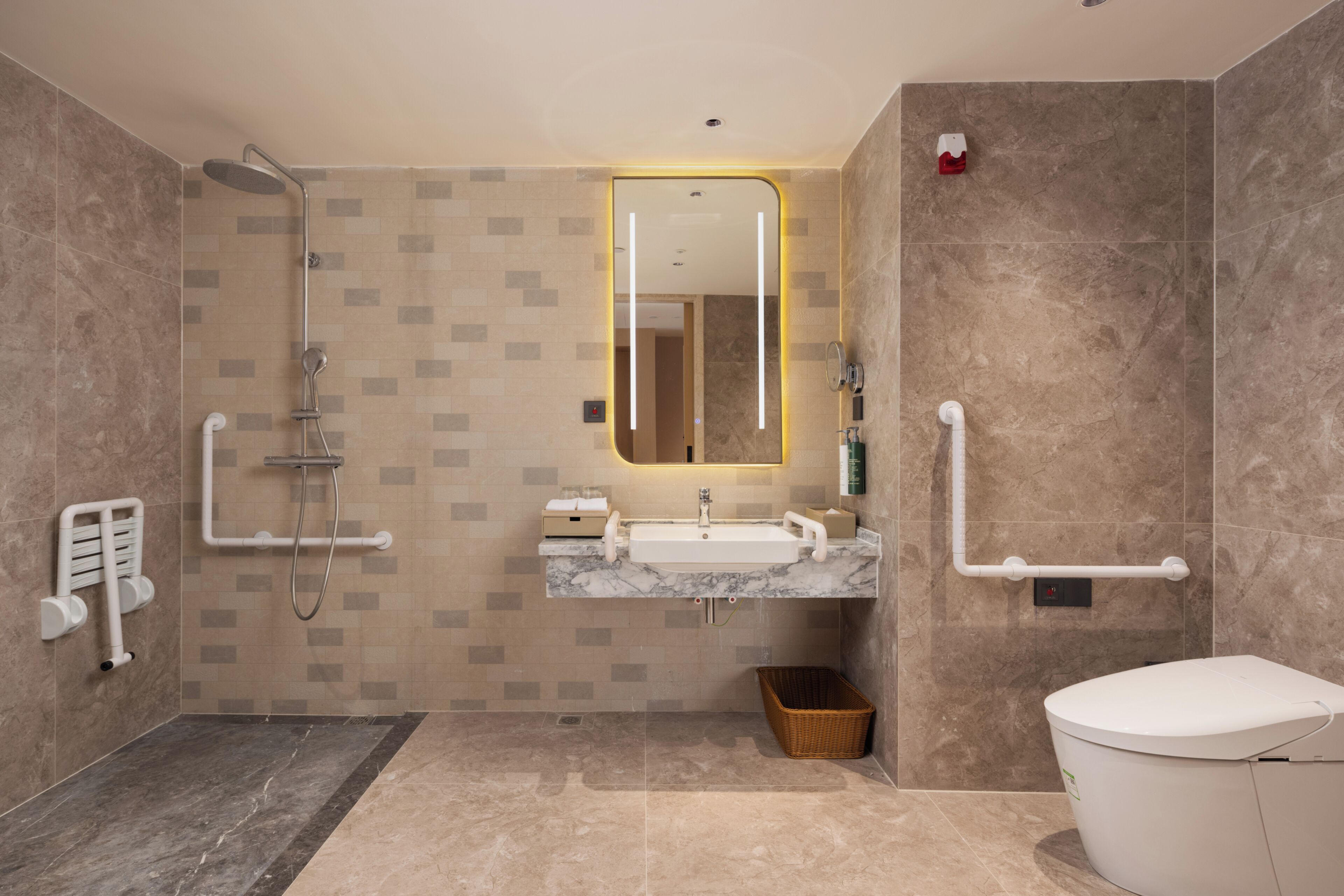 Un baño moderno con ducha, inodoro y lavamanos, equipado con barras de apoyo y un secador de manos.