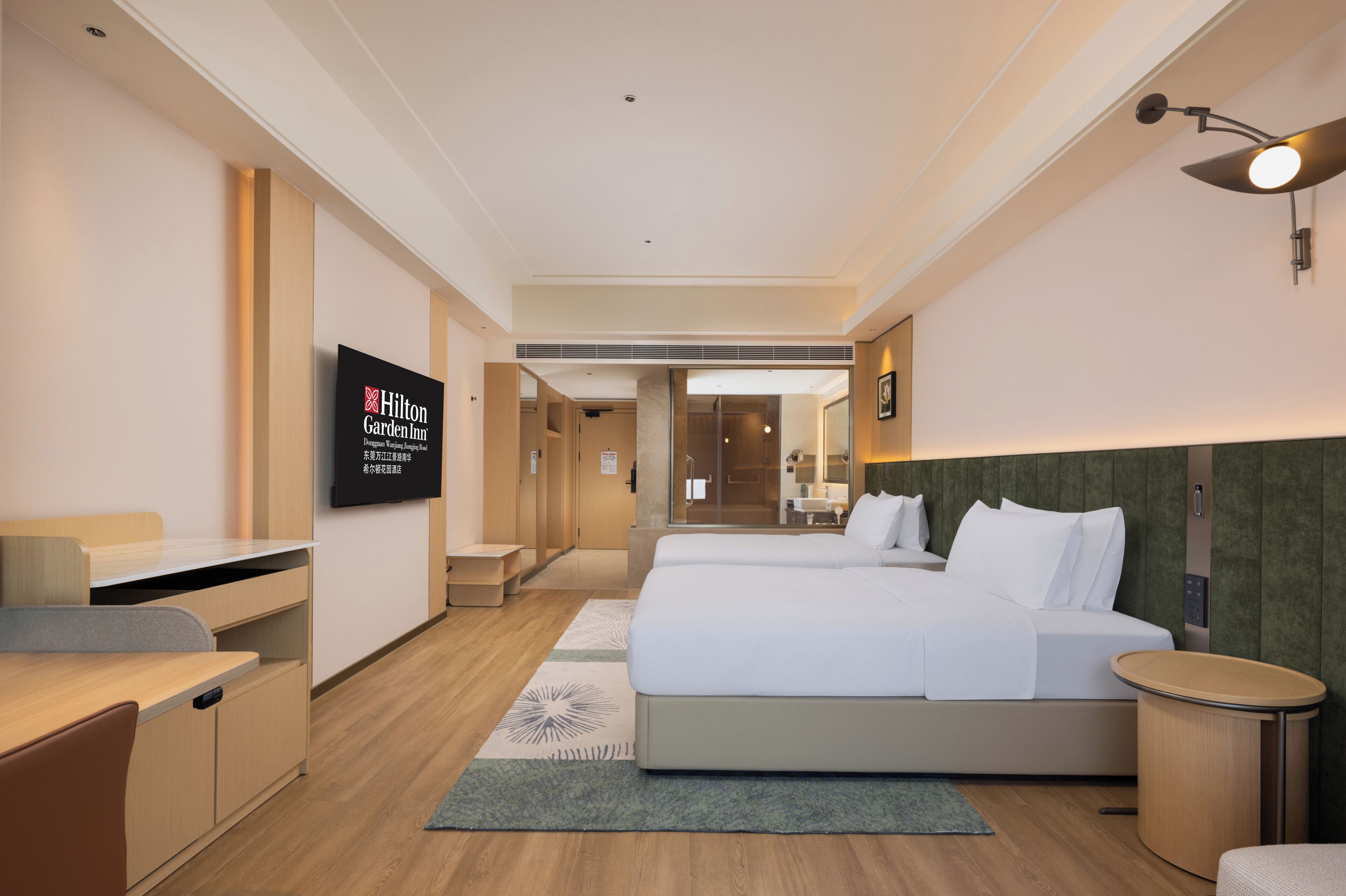 Habitación de hotel con cama, escritorio, silla, televisor y baño visible a través de una puerta abierta.