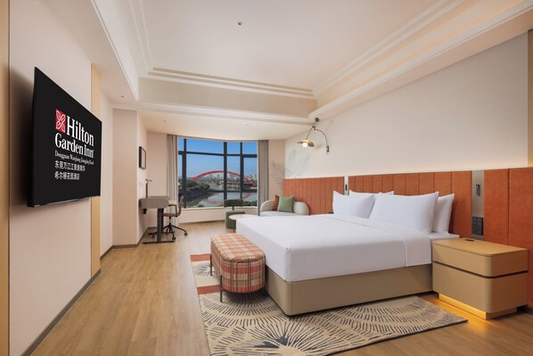 A modern hotel room with a large bed, a television, a desk, and a view of a cityscape. - Hilton Garden Inn Dongguan Wanjiang Jiangjing Road (Dongguan)