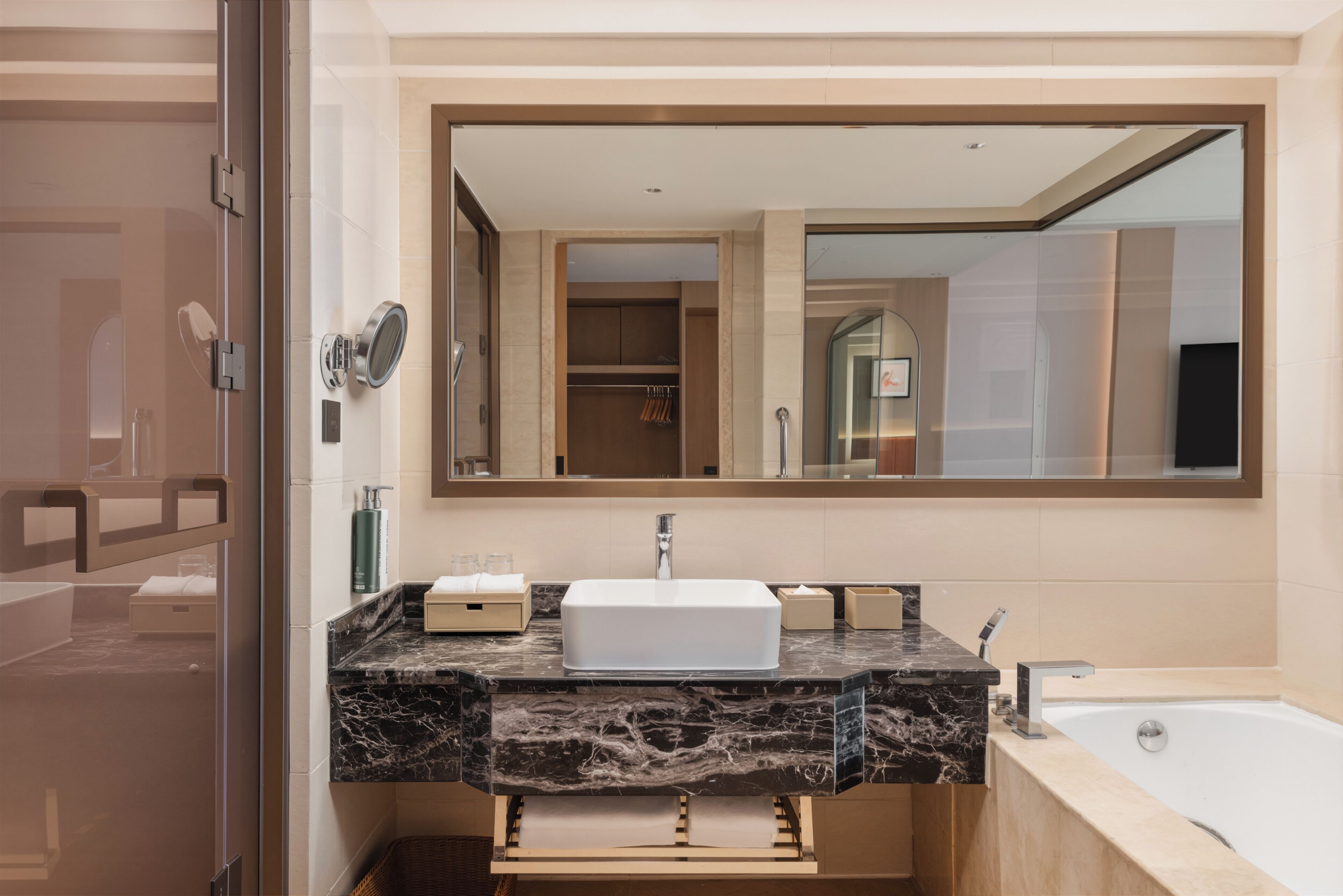 A modern bathroom with a marble sink, a large mirror, and a bathtub.