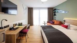 Ein Hotelzimmer mit Bett, Schreibtisch, Stuhl, Fernseher und Blick ins Freie.