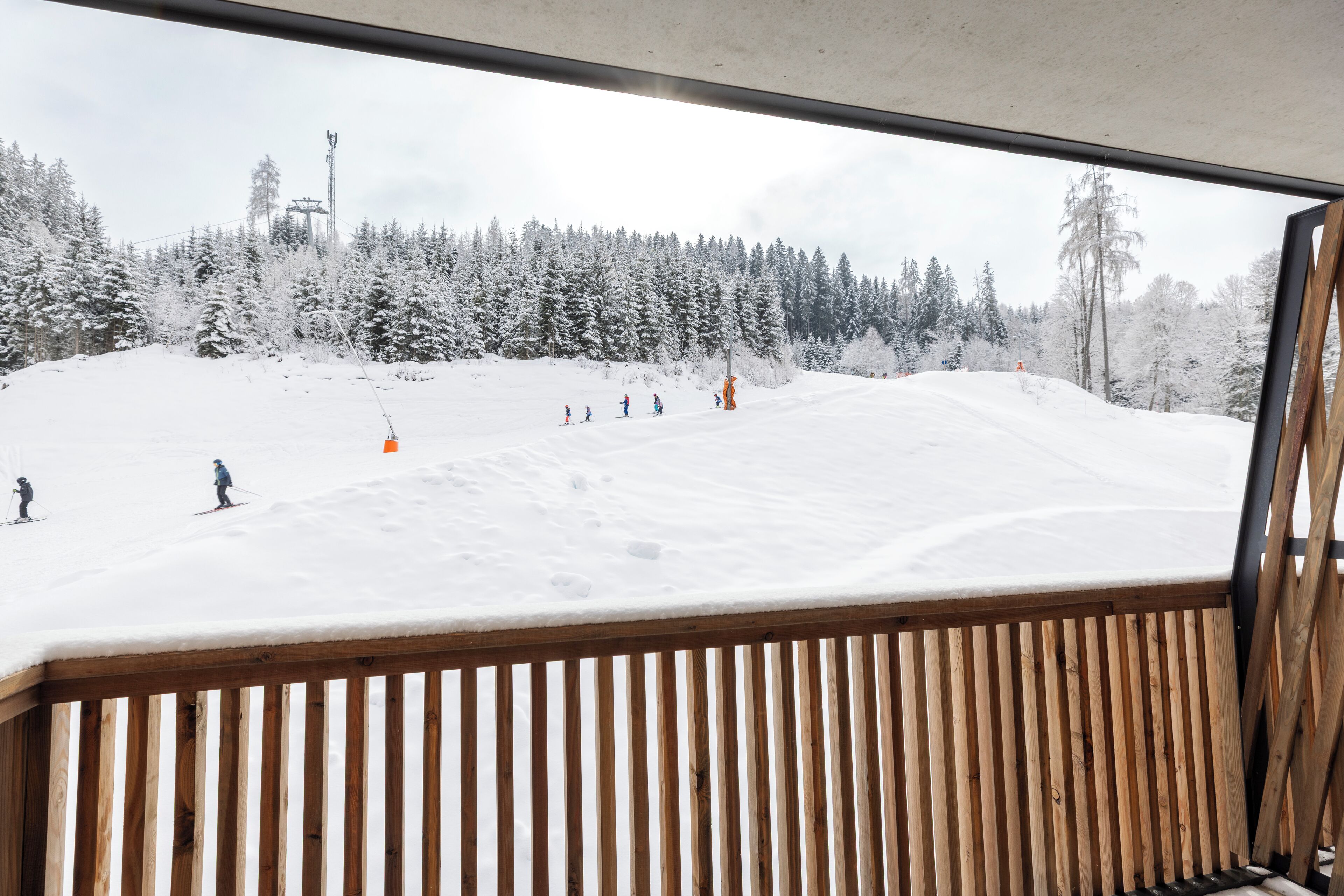 A view of a snowy ski slope through a window with wooden slats.