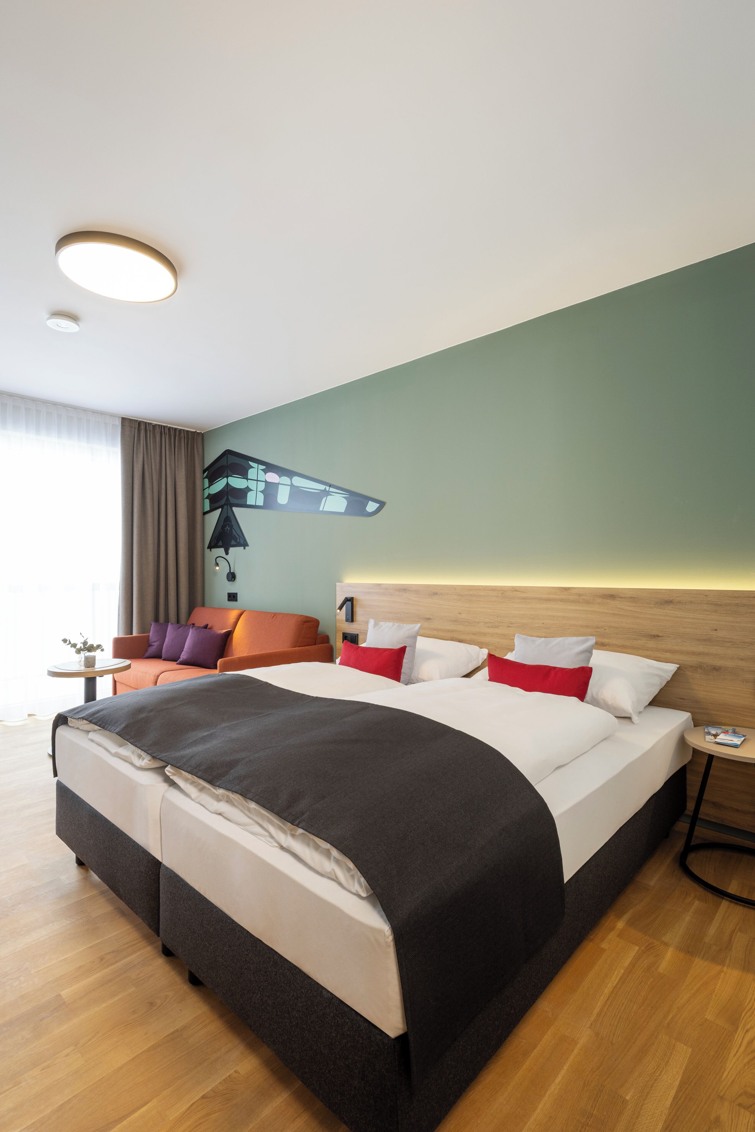A hotel room with a large bed, a sofa, a small table, and a wall-mounted light fixture.