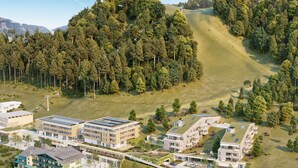 Ein moderner Wohnkomplex mit mehreren Gebäuden, begrünten Dächern und bewaldeten Hügeln im Hintergrund.