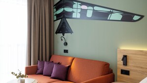 Ein Hotelzimmer mit einer Couch, einem kleinen runden Tisch mit einer Vase, einem Bett, einer Wandlampe und einem hölzernen Kopfteil.