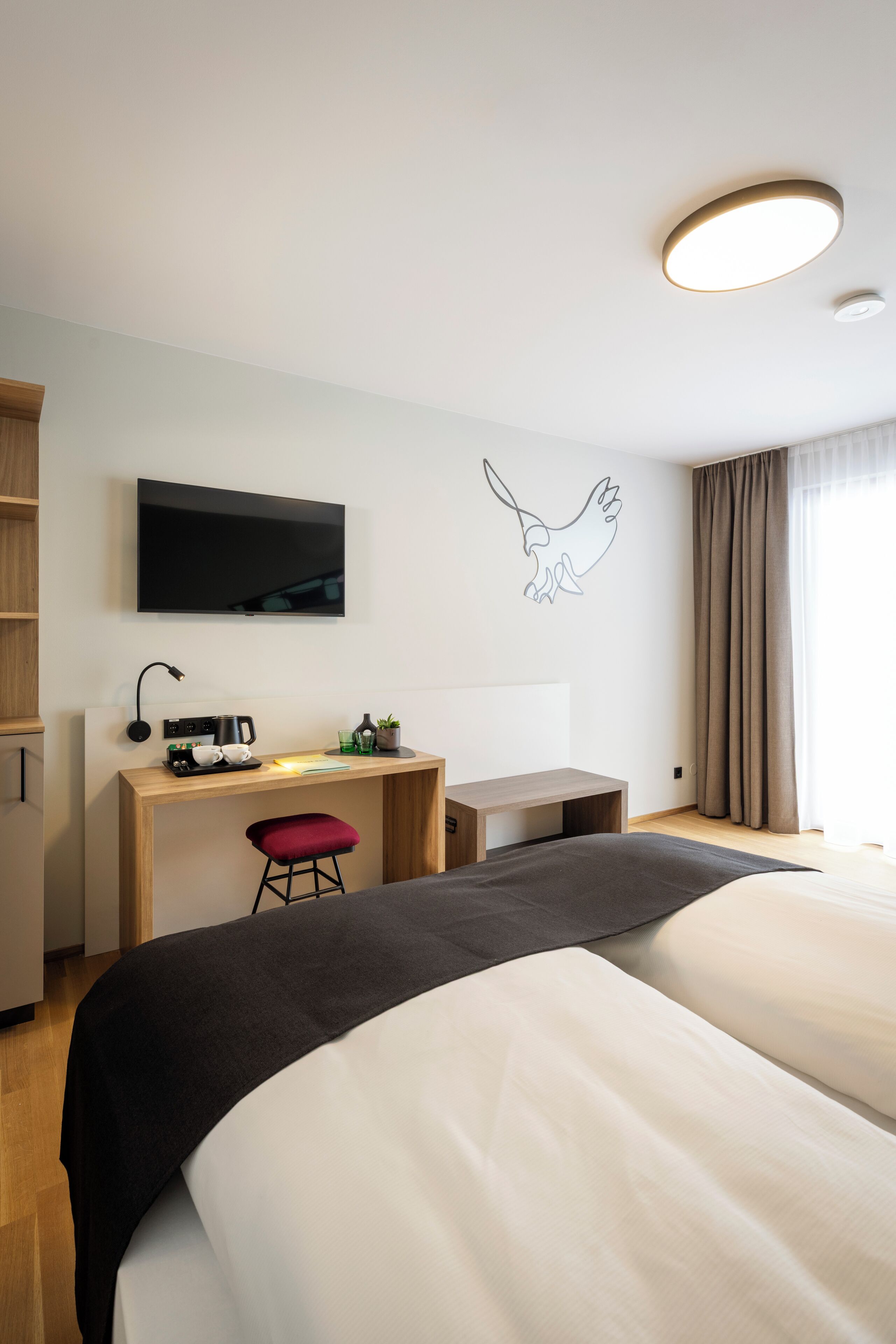 A hotel room with a bed, a desk, a chair, a television, and a wall-mounted artwork.