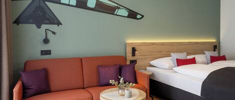 Una habitación de hotel con un sofá, una mesita redonda, una cama y un mural en la pared.