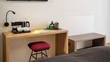 A modern hotel room with a wooden desk, a flat-screen TV, a red cushioned stool, and a wall art of a bird.