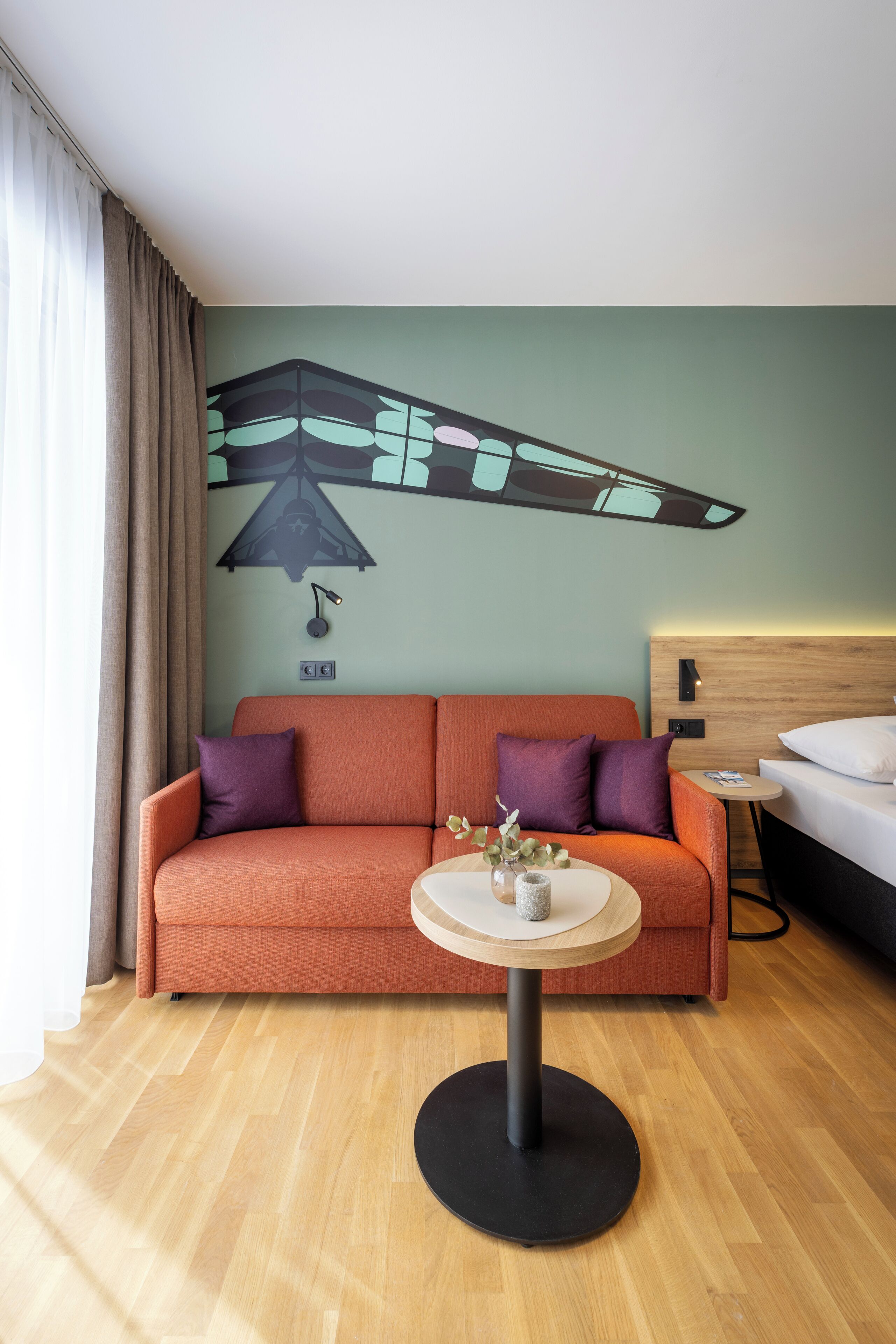 Una habitación de hotel con sofá, una mesa redonda, una cama y una obra de arte en la pared.