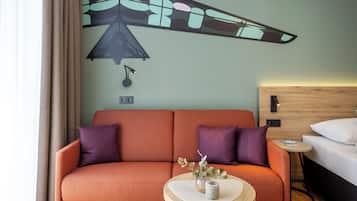 A hotel room with a sofa, a round table, a bed, and a wall art piece.