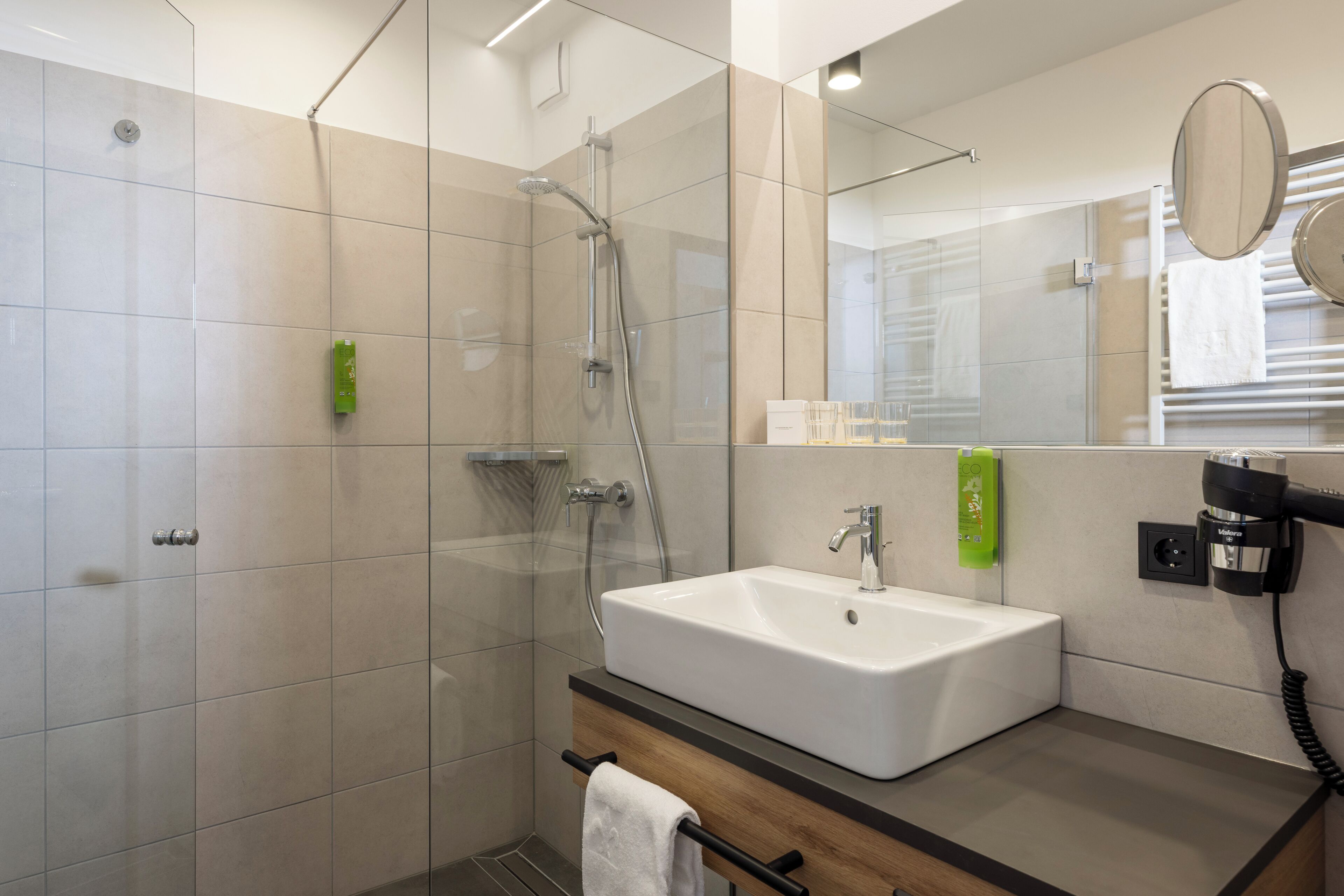 Un baño moderno con ducha acristalada, lavamanos blanco y espejo.