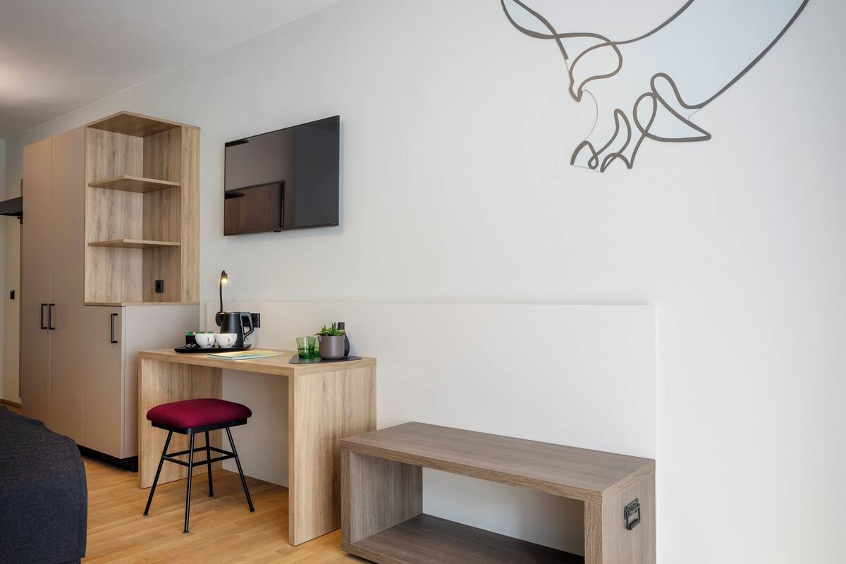 Een moderne kamer met een houten bureau, een rode kruk, een flatscreen televisie aan de muur en een houten bank.