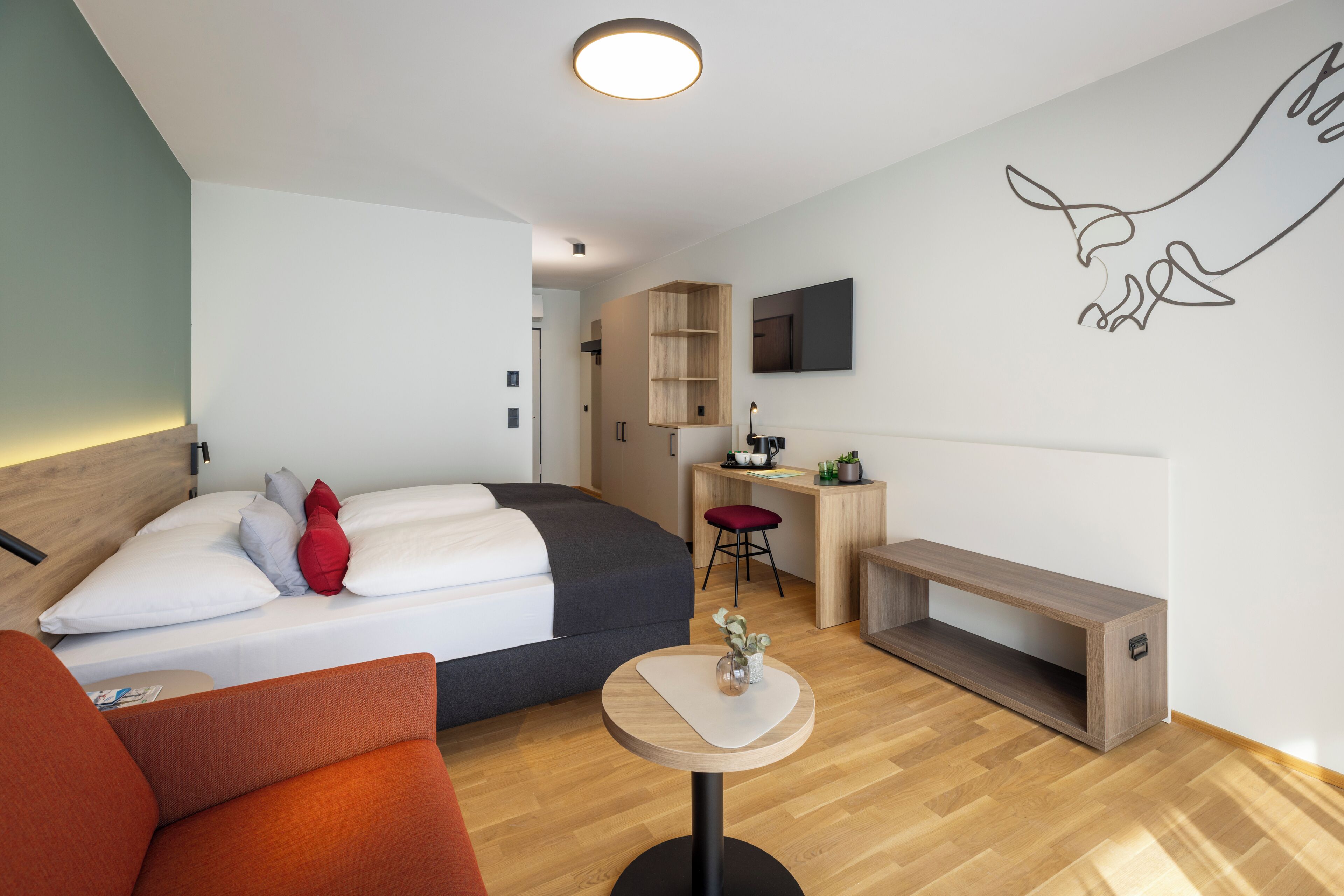 Ein modernes Hotelzimmer mit Bett, Schreibtisch, Stuhl und einem kleinen Tisch.