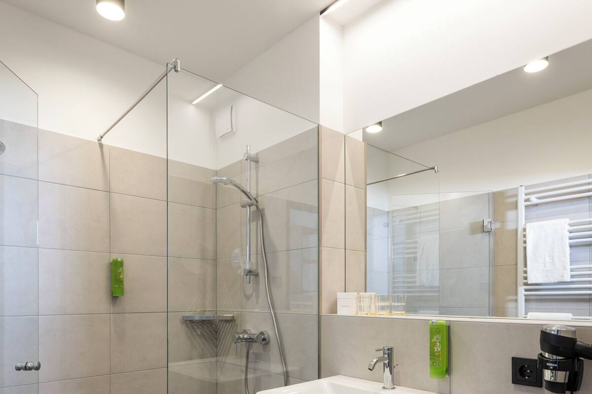 Een moderne badkamer met een glazen douchecabine, een wit wastafelmeubel en een spiegel erboven.