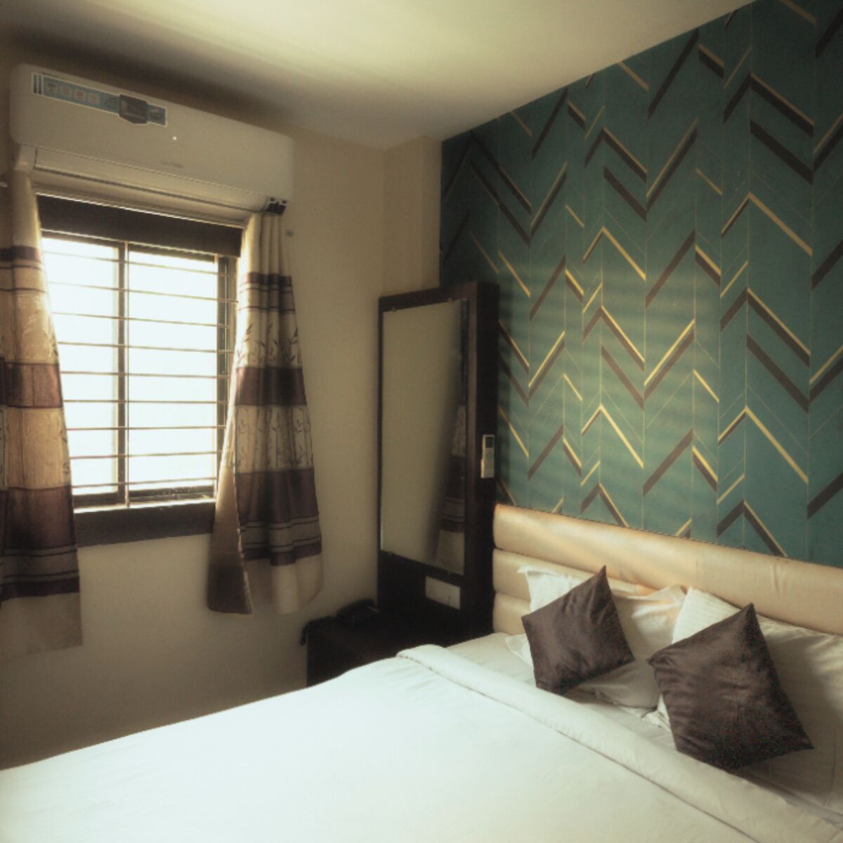 Una habitación de hotel con una cama, una ventana con cortinas, un espejo y una pared con un diseño geométrico.