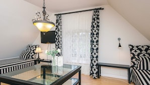 A modern loft bedroom with a glass dining table, black and white striped furniture, a chandelier, and a large window with patterned curtains. - 4 Star Holiday Home in Skanderborg (Skanderborg)
