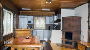 Interior rústico de cabana com mesa de jantar de madeira, lareira de tijolos e área de cozinha com eletrodomésticos modernos.