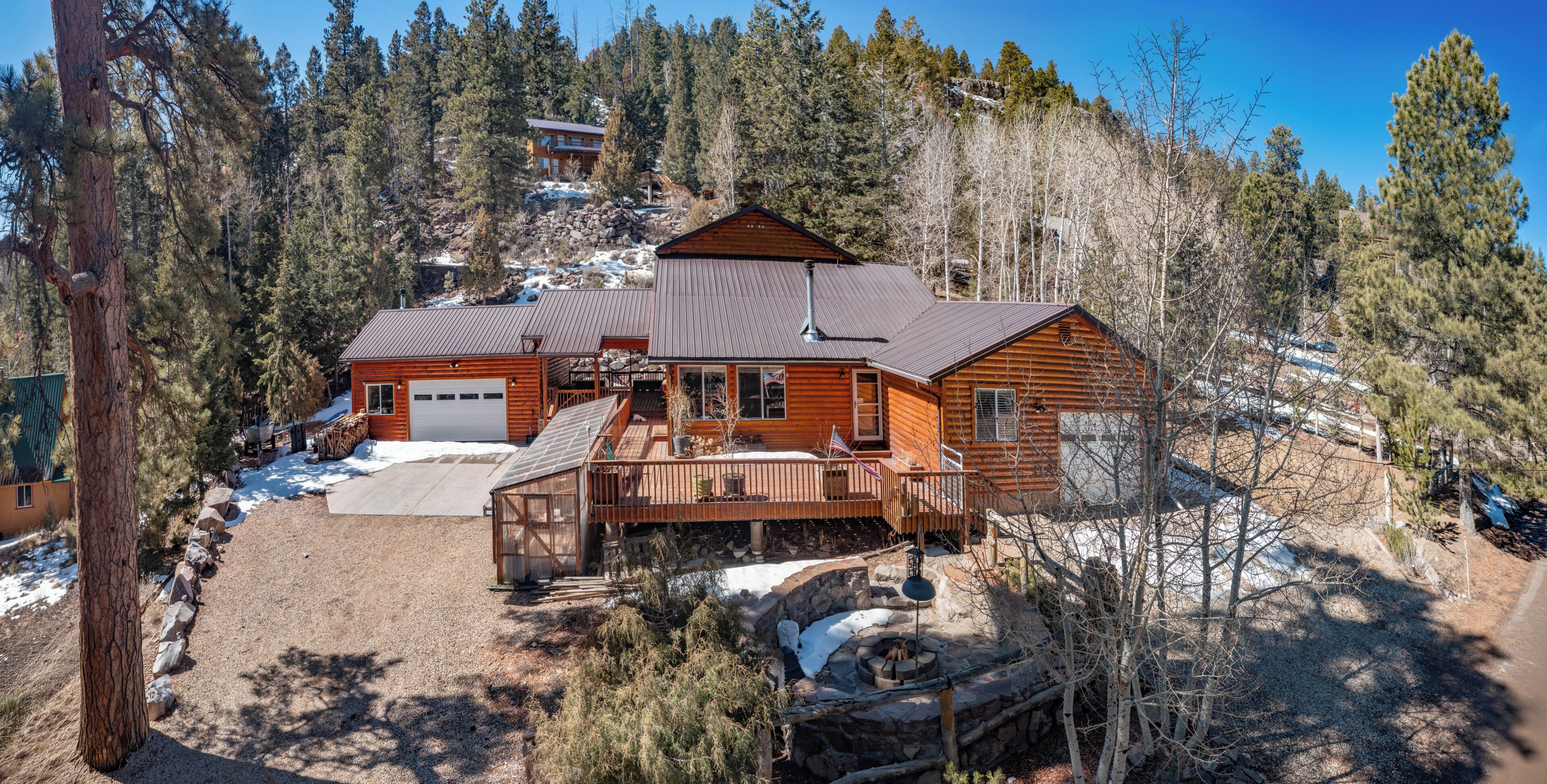 A log cabin with a deck, a garage, and a stone fire pit.