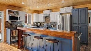Cocina con techo de madera, una isla central con taburetes, electrodomésticos integrados y salpicadero de azulejos.