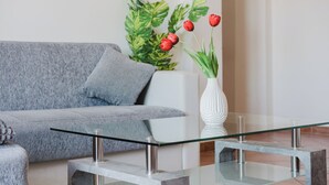 A modern living room with a grey sofa, a glass coffee table, and a white vase with red tulips.