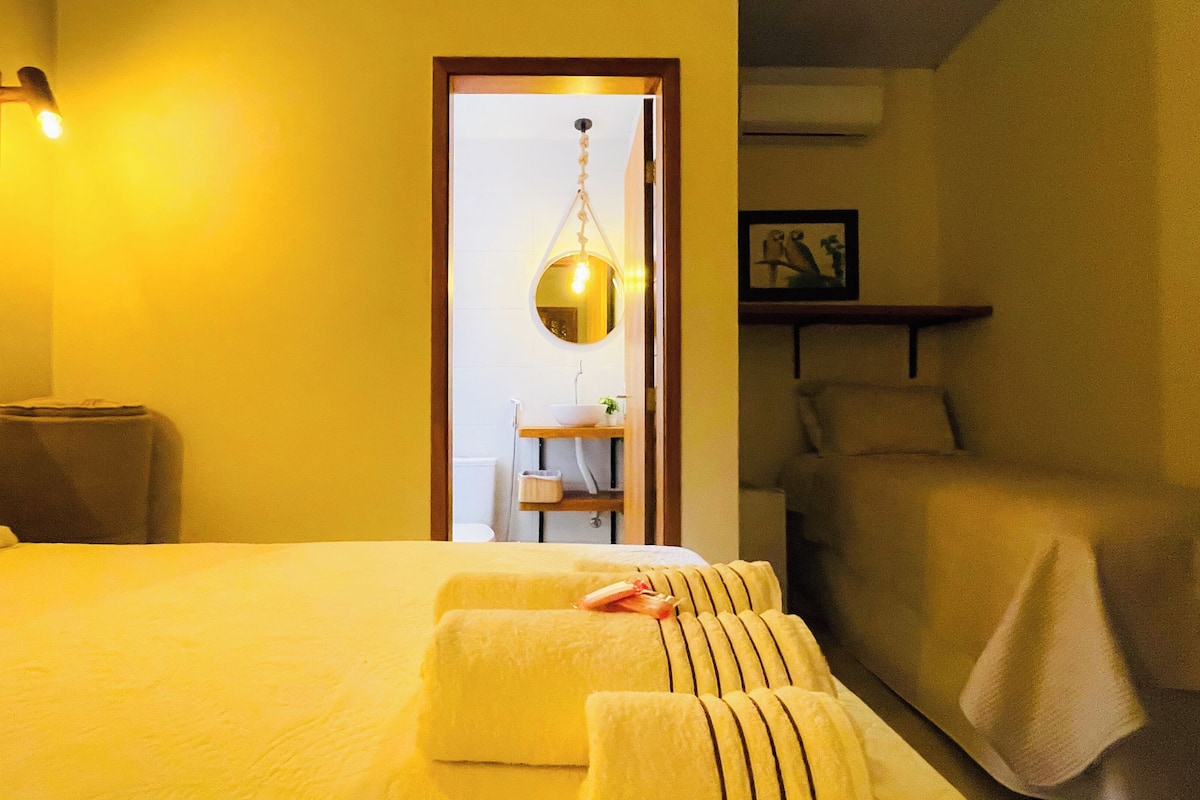 Ein Hotelzimmer mit Bett, Nachttisch, Stuhl, einer Pendelleuchte und einem gerahmten Bild an der Wand.