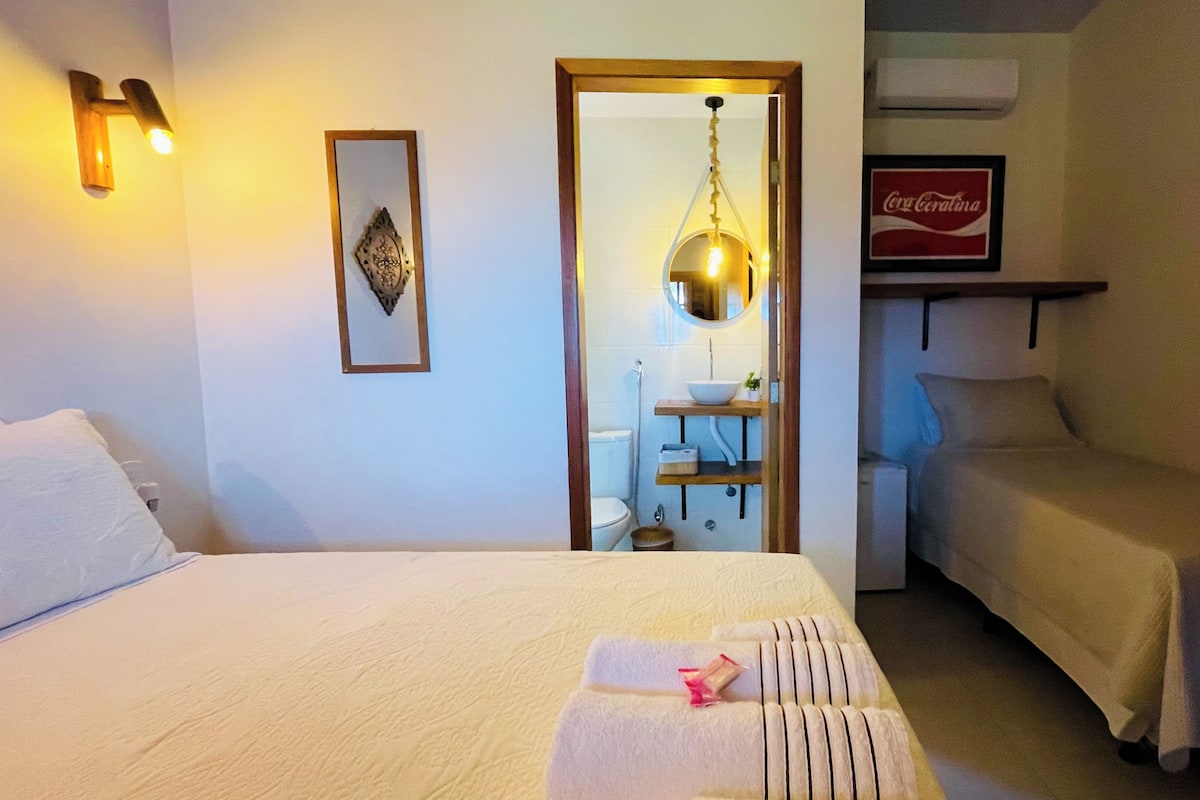 Ein Hotelzimmer mit zwei Betten, einem Badezimmer, einem Coca-Cola-Schild und einer Hängelampe.