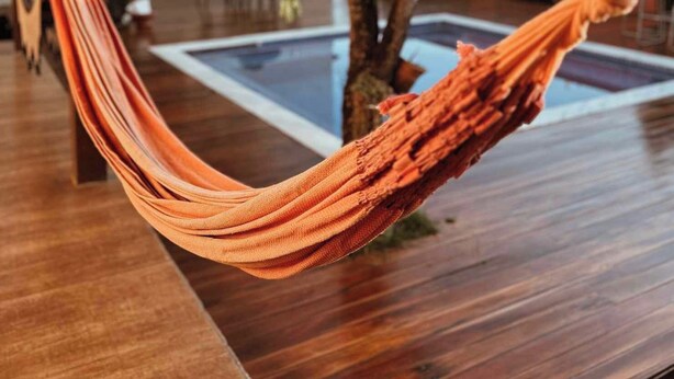 A hammock under a wooden pergola with a pool and a tree in the background. - Vila Bonita Guest House (Alto Paraíso de Goiás)