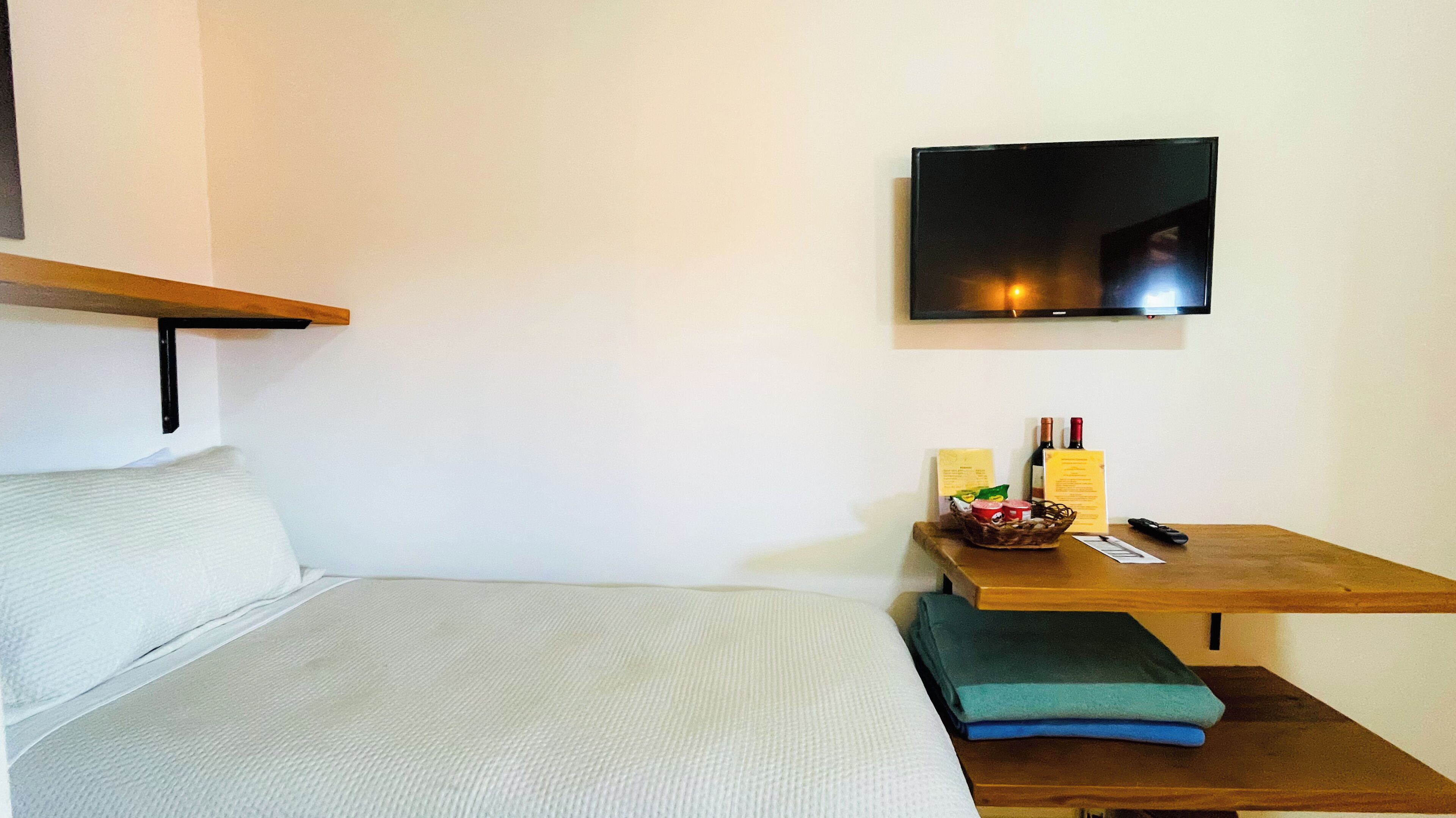 Une chambre à coucher avec un lit, une table de chevet sur laquelle se trouve un panier, une télécommande et une bouteille de vin.